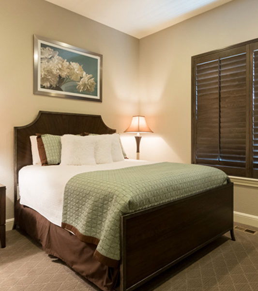 guest bedroom with green bedding and room darkening hunter douglas dark wood window shutters in Denver