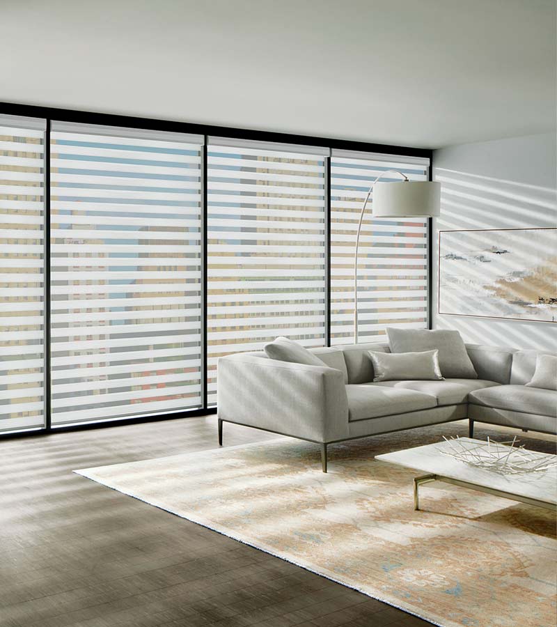 Designer Banded Sheer Shades in a living room with a couch and lamp. The sheer shades are covering black trim windows