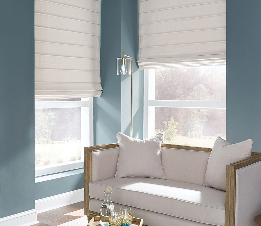 cream fabric custom roman shades in corner window blue walls and settee