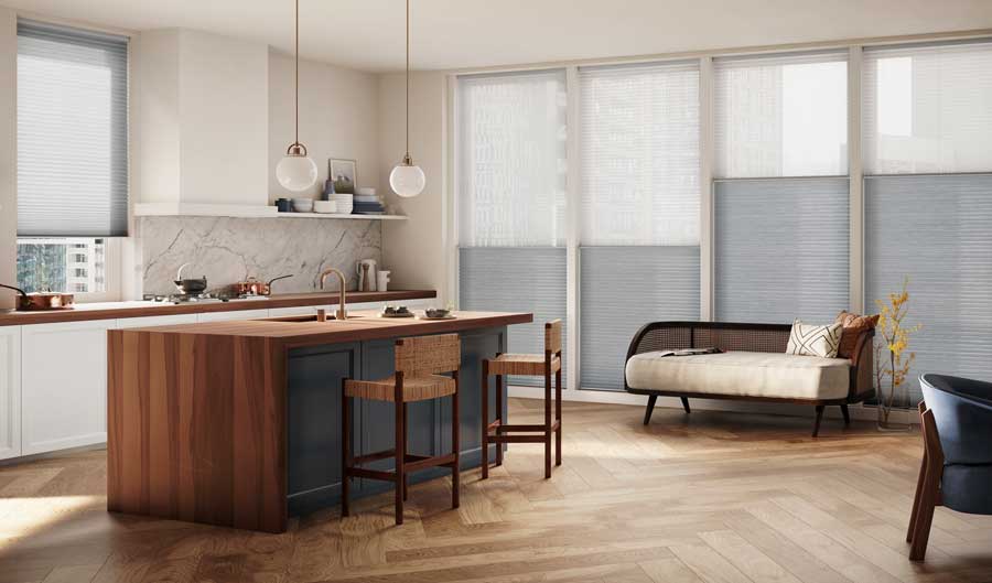 A kitchen area with a wooden island, chaise lounge in the corner and floor to ceiling windows with Applause® Honeycomb Shades covering the windows