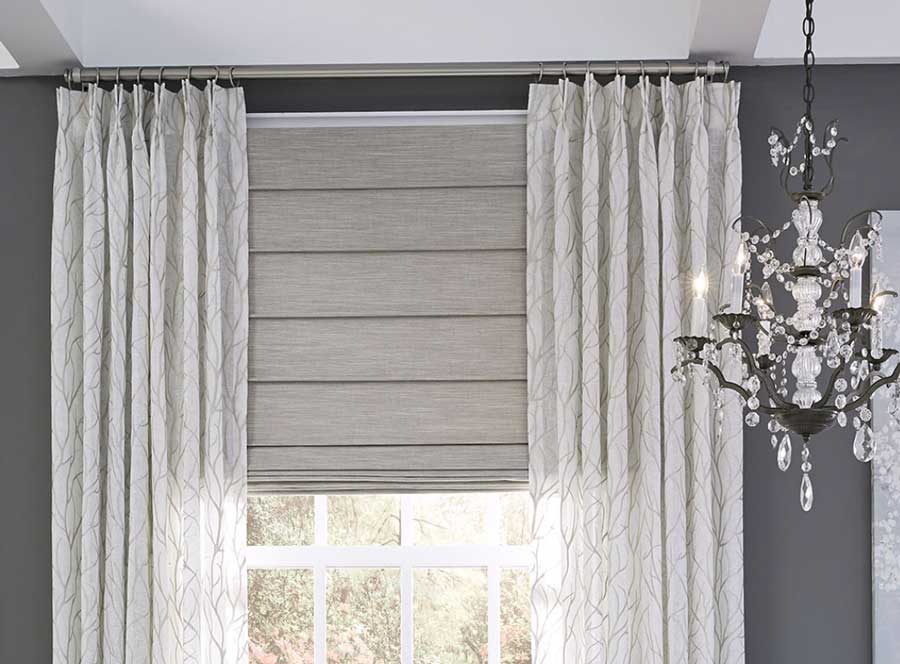 Pinch Pleat Drapery with Custom Roman Shade on white trim windows against a dark gray wall with a chandelier hanging from the ceiling