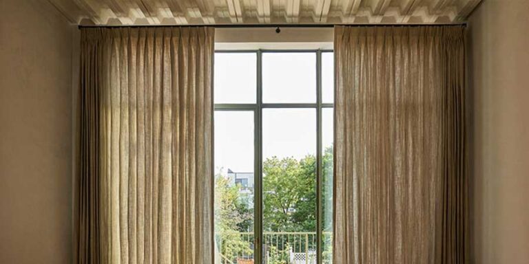pinch pleat drapery on either side of floor to ceiling windows that overlook greenery