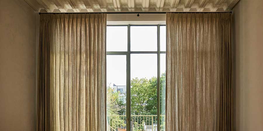 pinch pleat drapery on either side of floor to ceiling windows that overlook greenery