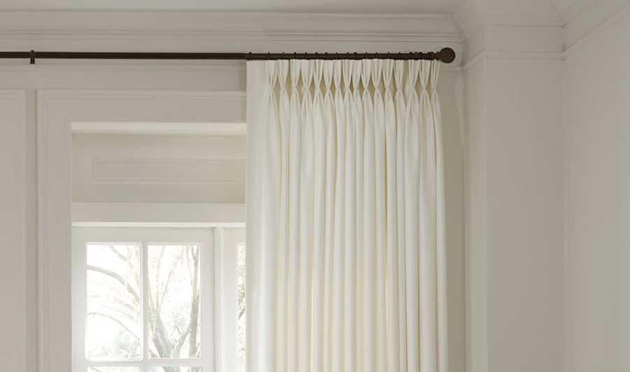 Triple Pleat, Pinch Pleat Drapery on a black curtain rod against a white trim window with a tan wall behind it