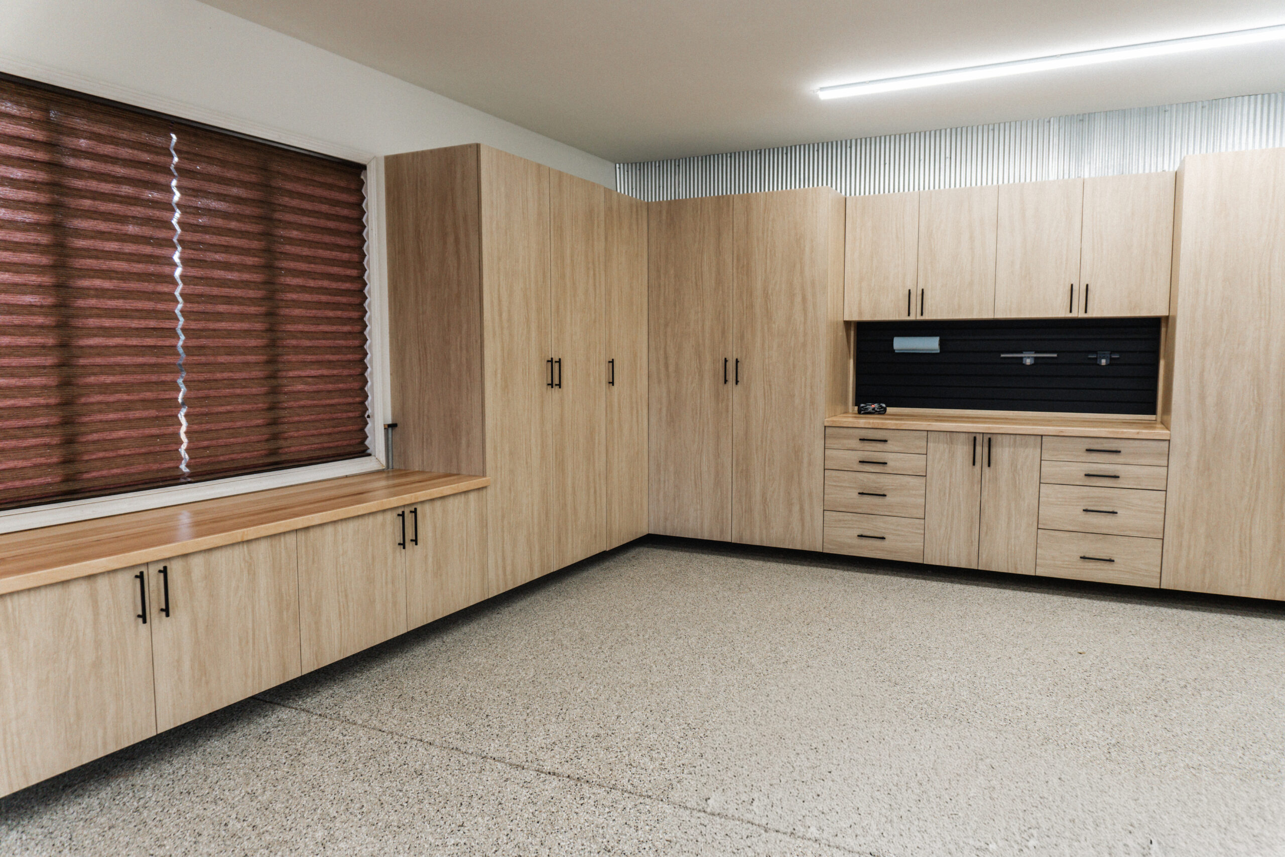 Custom garage cabinetry with Duette honeycomb shades creating organized storage and energy efficiency